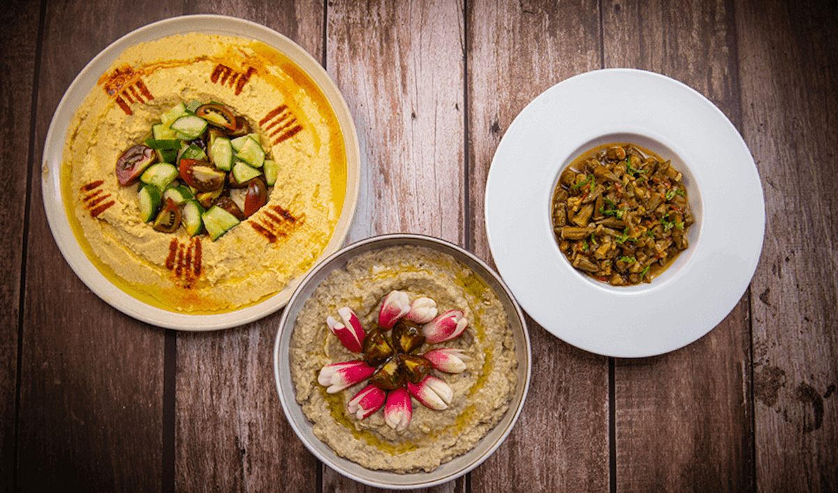 Three bowls of hummus on a wooden table.