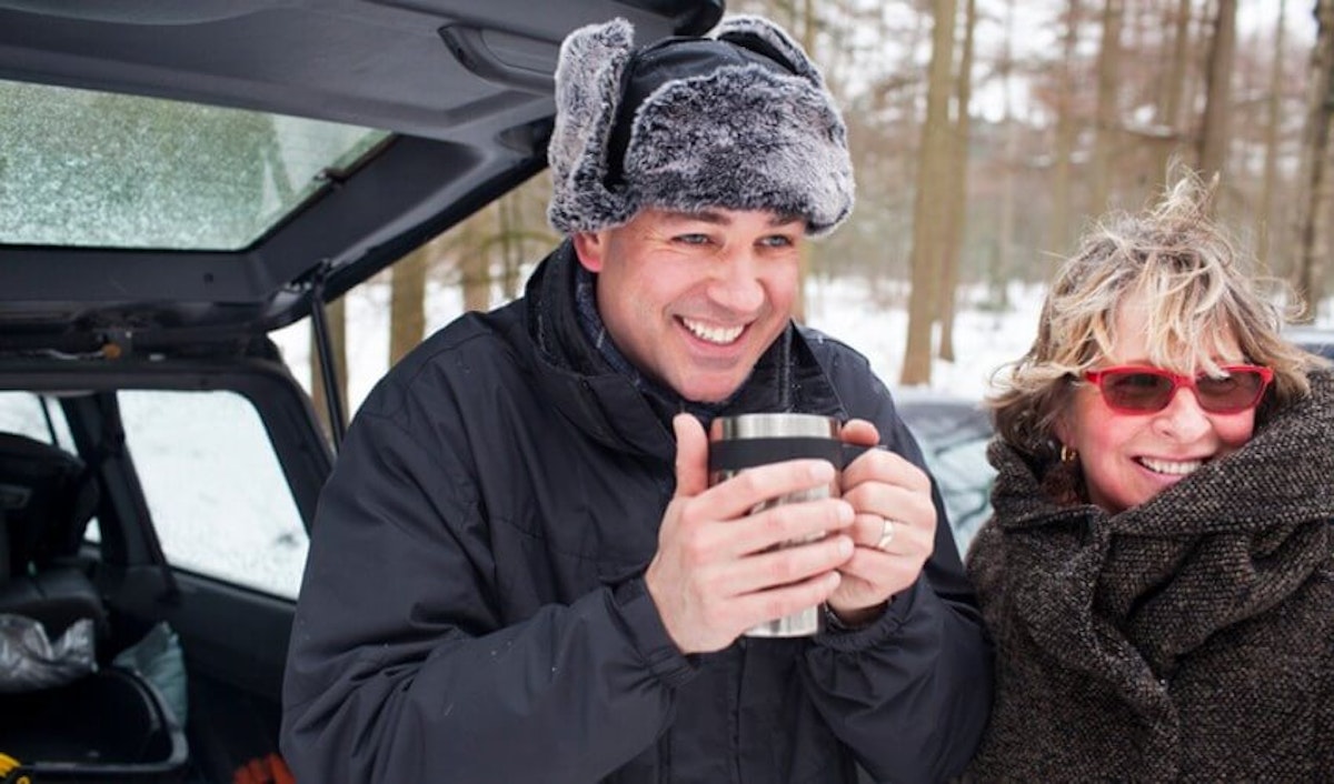 A man and woman holding a cup of coffee in the back of a car.