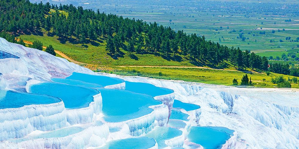 Vibrant blue terraced thermal pools in a lush green landscape.