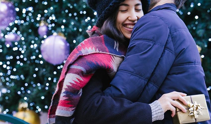 A man and woman hugging in front of a christmas tree.