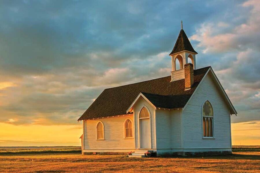 A white church in the middle of a field at sunset.