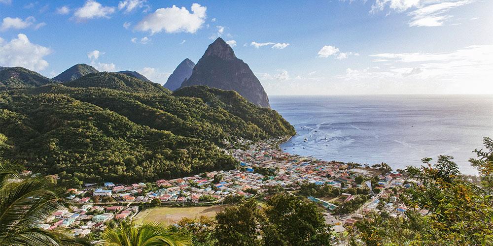 Scenic view of a tropical coastal village with towering peaks in the background.
