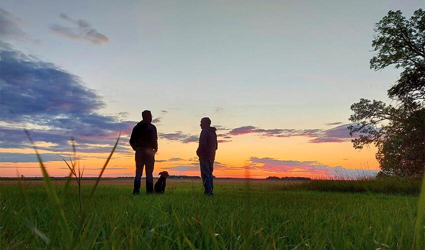 Two men standing in a field at sunset.