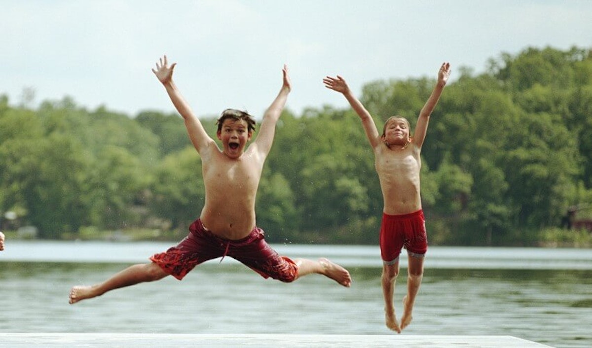 Three boys jumping off a dock on a lake.