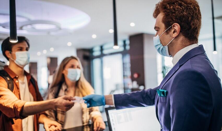 A man in a mask is shaking hands with a woman at a hotel.