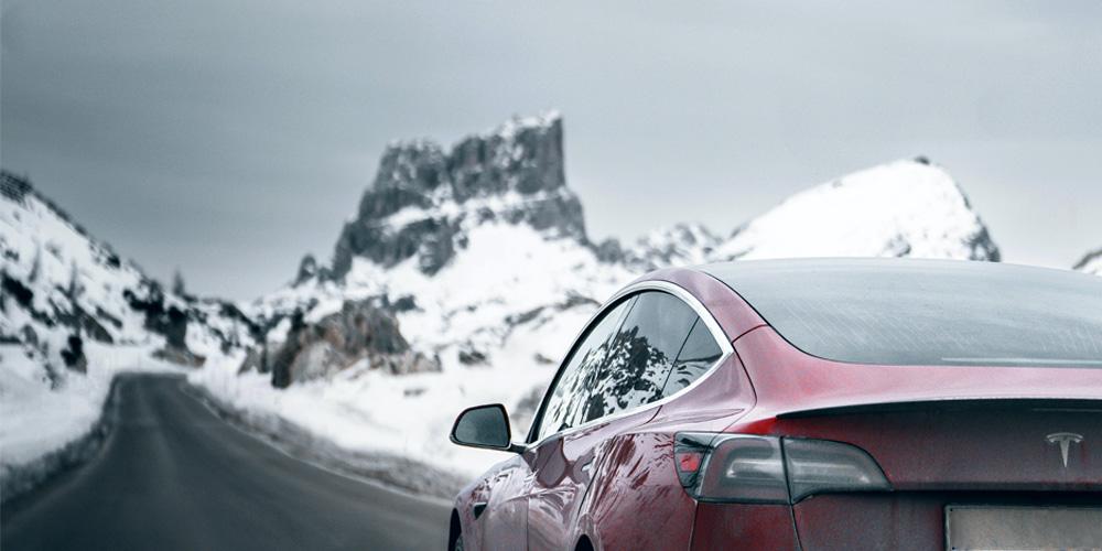 A red tesla car on a snowy mountain road.