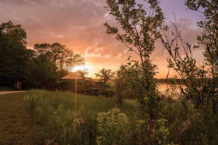 The sun is setting over a lake in a wooded area.
