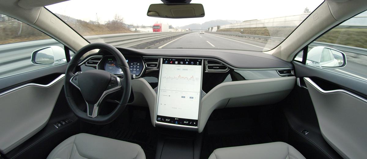 The interior of a self-driving car; the driver's seat and passenger seat are empty as the car makes its way down a highway.
