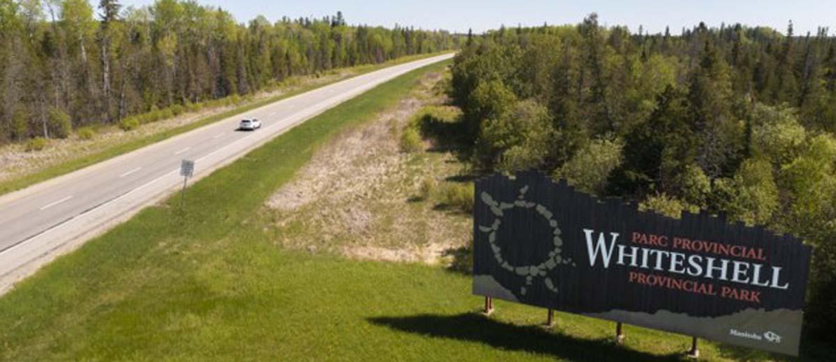 An aerial view of a road with one car driving on it and a sign off to the right side that says Whiteshell Provincial Park