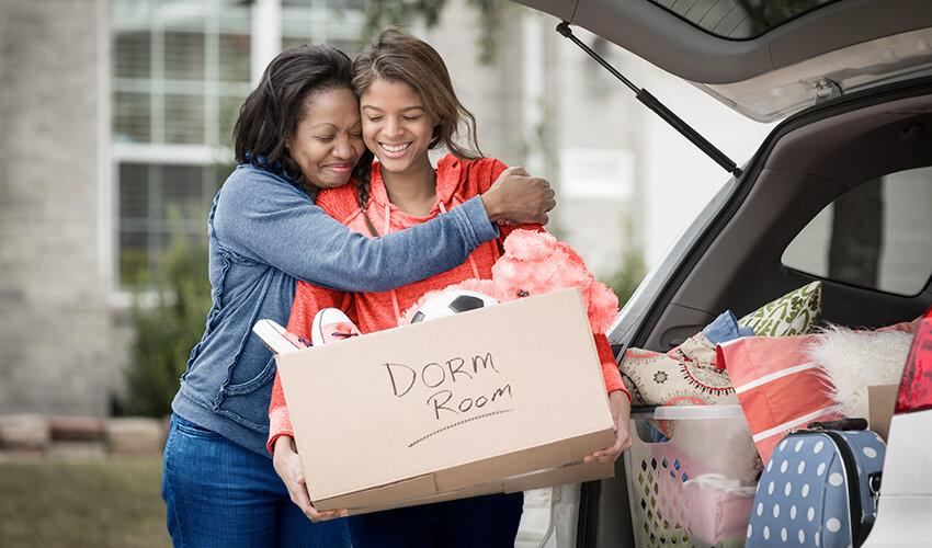 Two women hugging in the trunk of a car with a box of toys.