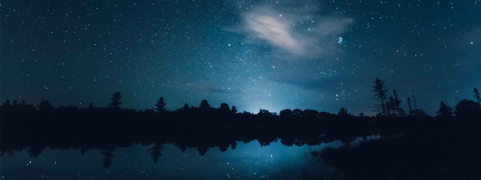A night sky filled with stars over a lake lined with trees.