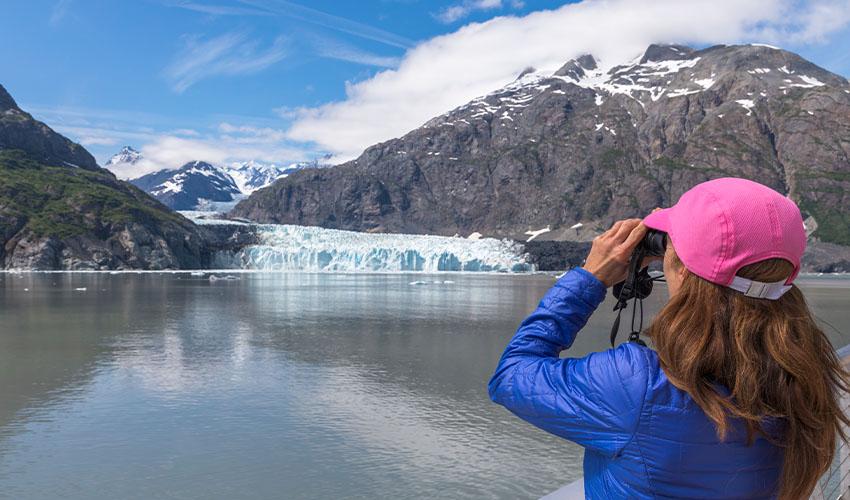 Someone on the deck of a cruise ship looking at a snow-capped mountain in the distance.
