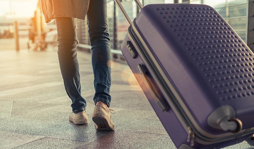 A woman is walking with a purple suitcase.