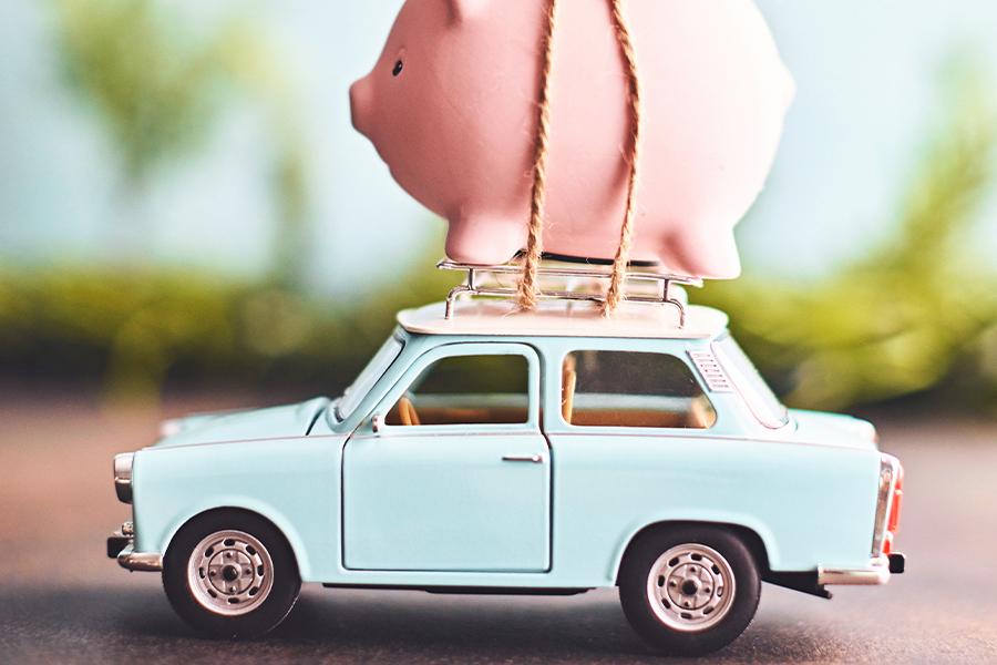 A toy car carrying a pink piggy bank secured with string on its roof.