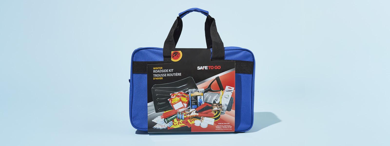 A dark blue roadside safety kit, with black handles and a label that shows the different products inside of it, sitting upright on a light blue surface.