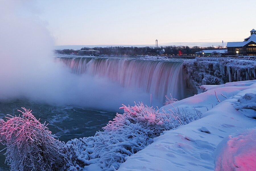 A frosty morning at niagara falls with snow-covered vegetation and mist rising from the cascading water.