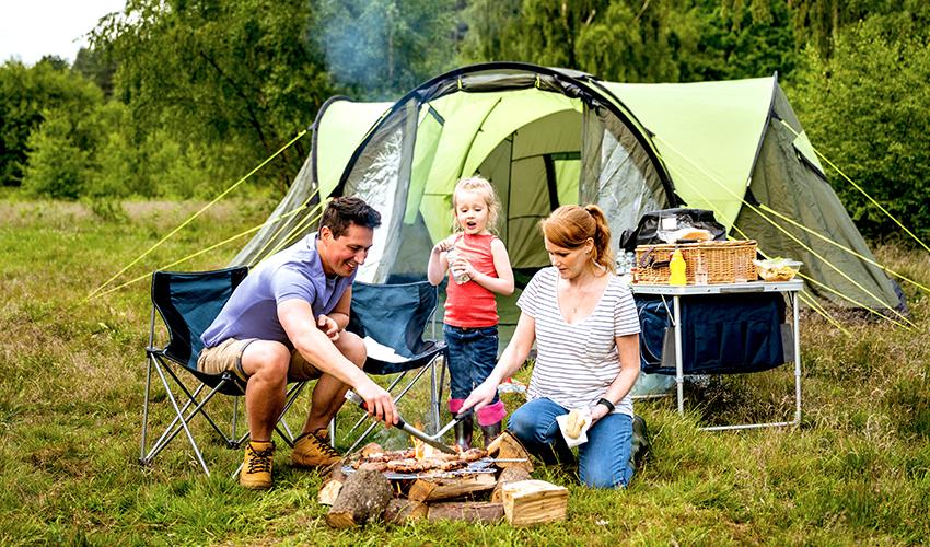 A family of three at a campsite, roasting dinner over a campfire.