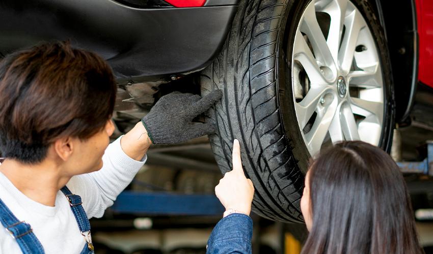 A man and woman inspecting the tire of a car.