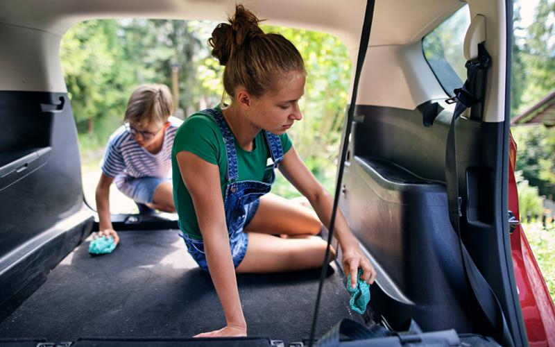 Two children holding cloth wipes cleaning the backseat of a car