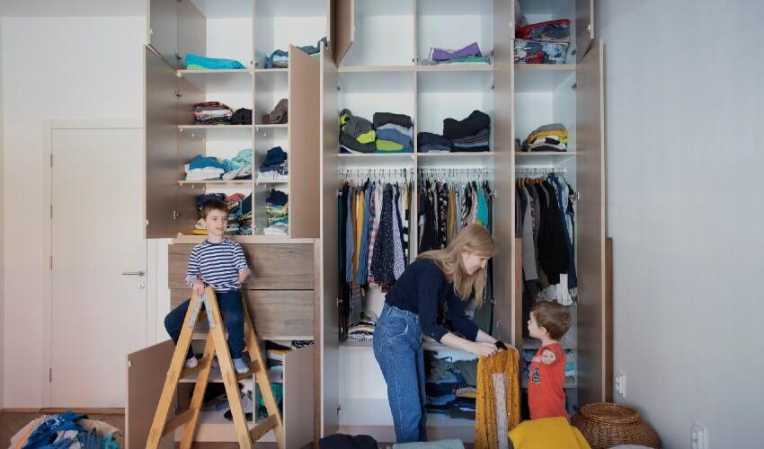 A woman and child are putting clothes into a closet.