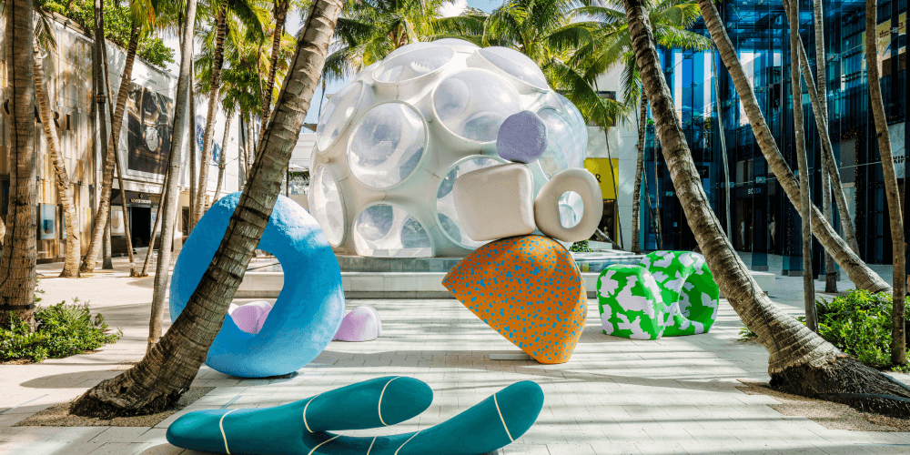 Modern art installation with abstract sculptures surrounded by palm trees in an urban plaza.