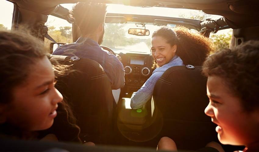 Family enjoying a road trip in a convertible car at sunset.