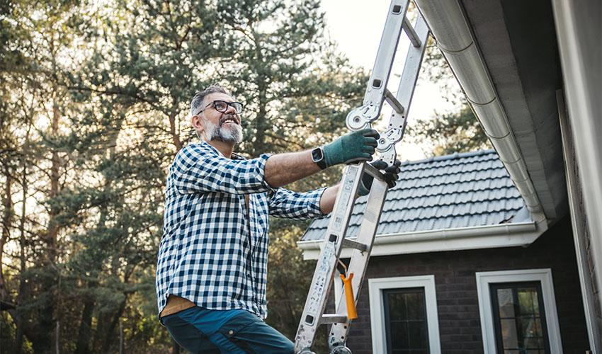 Man climbing a ladder outdoors to check a cottage roof.