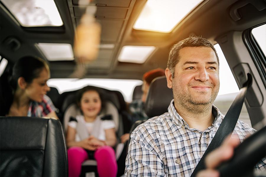 A man driving a car with his family in the back seat.