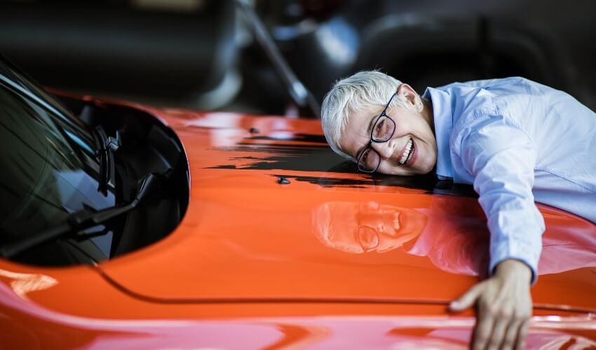 An older man leaning on the hood of a sports car.