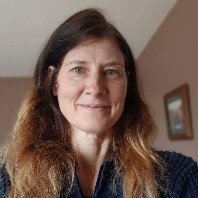 A headshot of a woman with long, brown hair wearing a blue sweater.