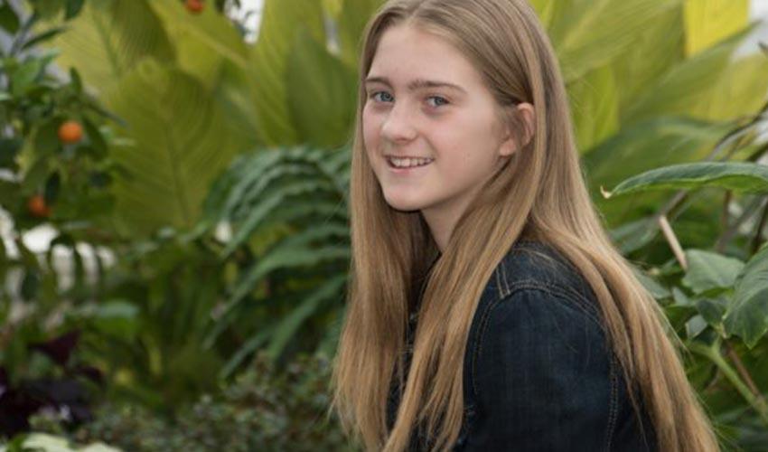 A young girl smiling in front of plants.