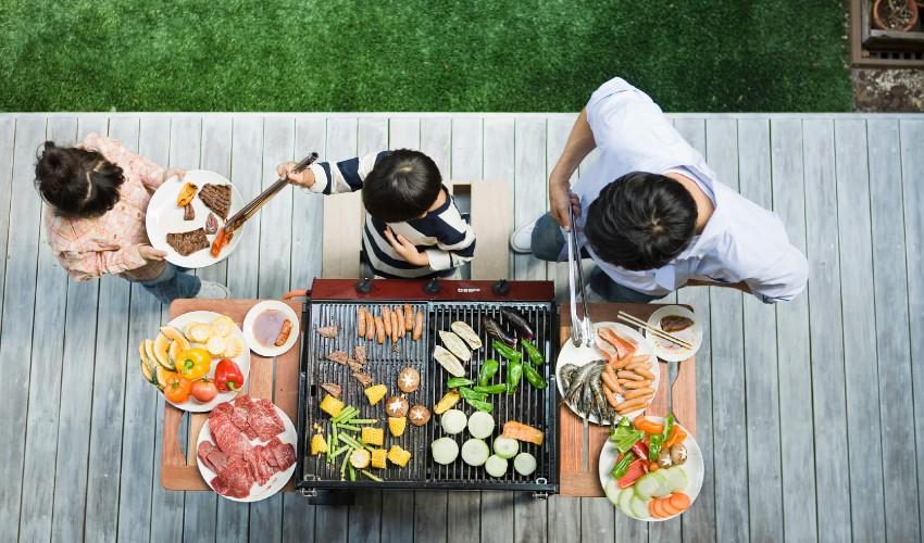 A family is preparing food on a grill.