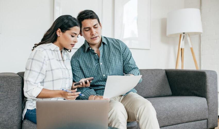 A man and woman sitting on a couch looking at paperwork.