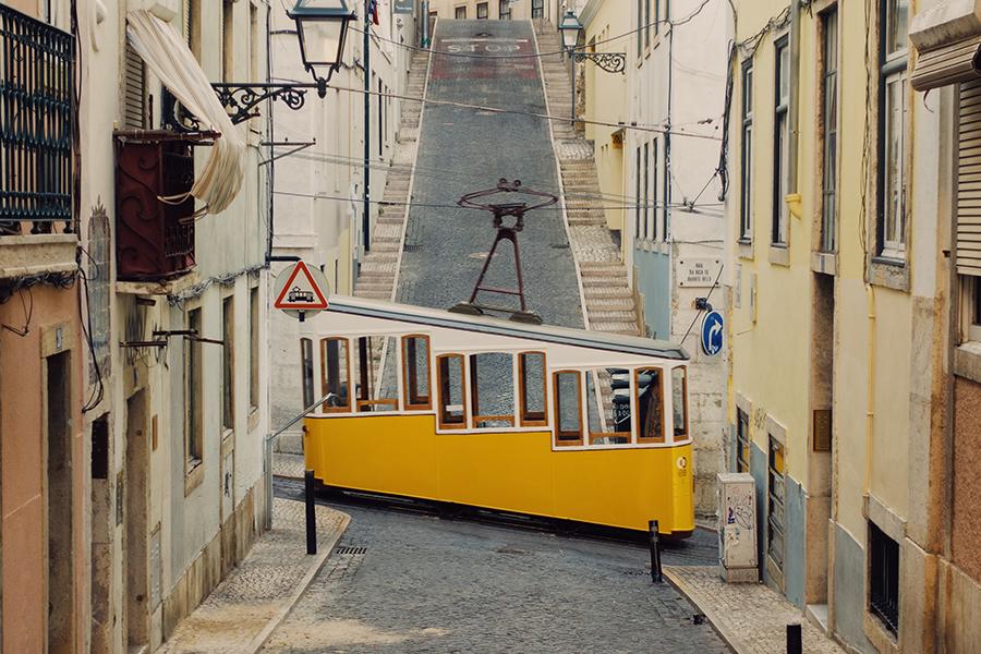 A yellow trolley car is driving down a narrow street.
