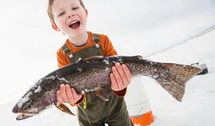 A young boy holding up a fish in the snow.