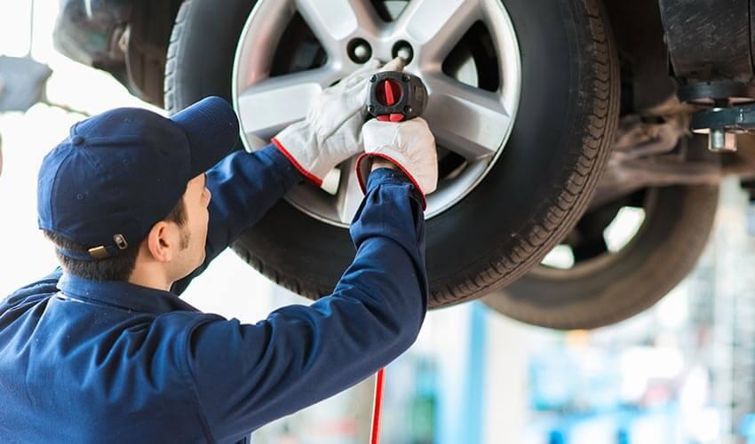 Mechanic using a pneumatic wrench to service a car's tire.
