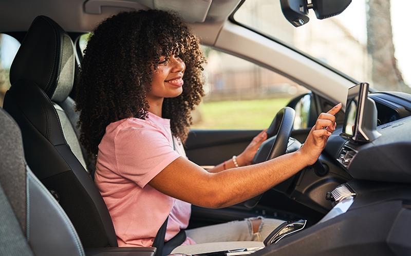 Woman sitting in a car with her hand touching navigation screen
