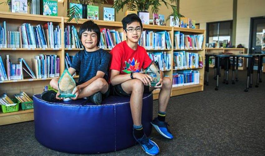 Two boys sitting on a purple bean bag in a library.
