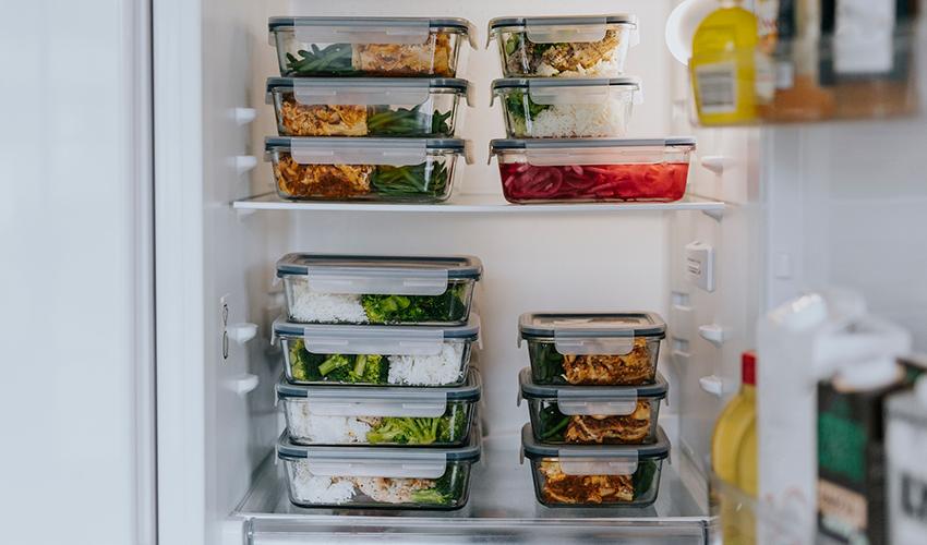 An open fridge with two shelves containing stacked glass meal prep containers.