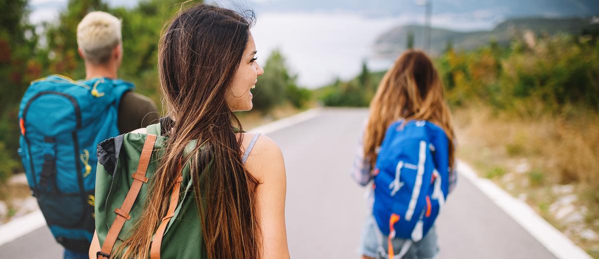 Three young people walking down an empty street; they are each wearing backpacks, signifying that they are travelling.