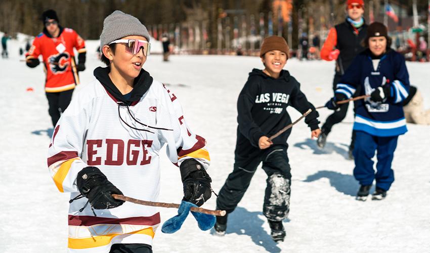 A group of children playing hockey in the snow.