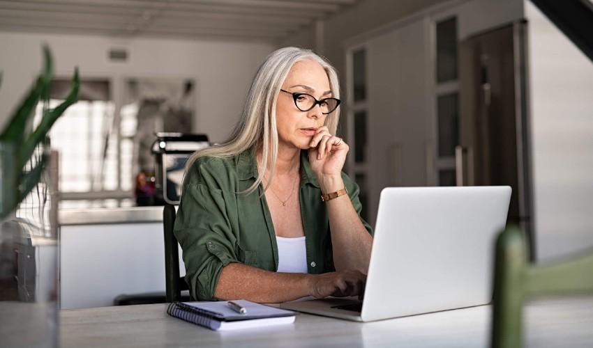 A woman sitting at a table looking at her laptop.