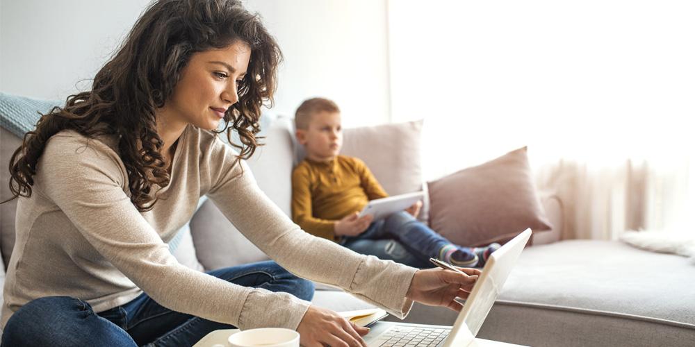 A woman using a laptop while sitting on a couch with her son.