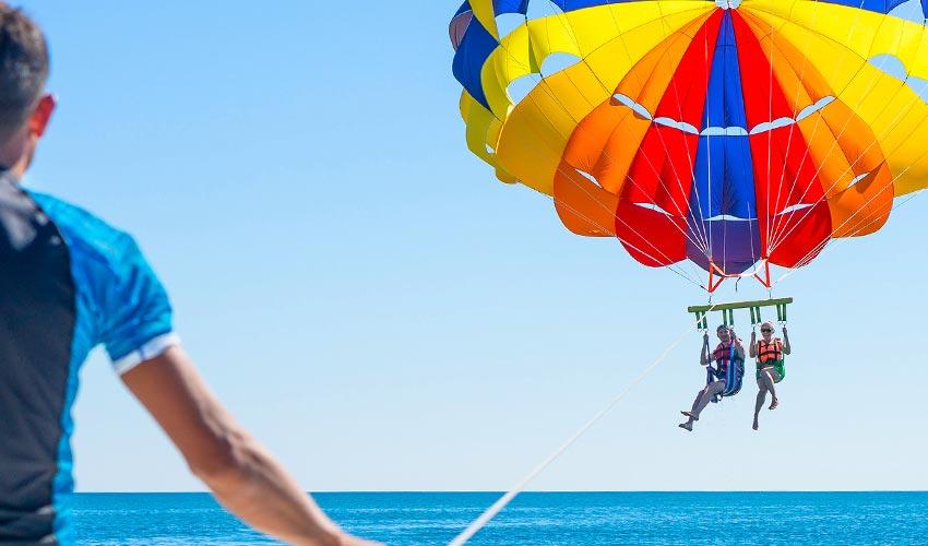 A man is parasailing over the ocean with a parachute attached to him.