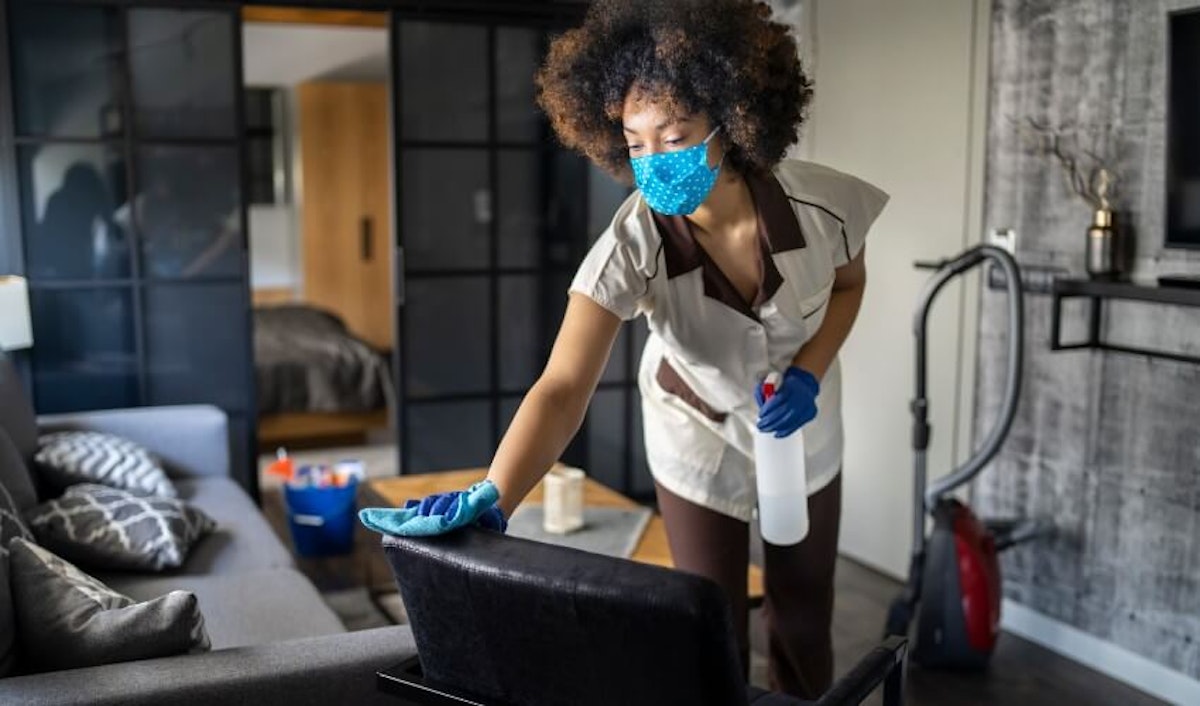 A woman wearing a face mask cleaning a living room.
