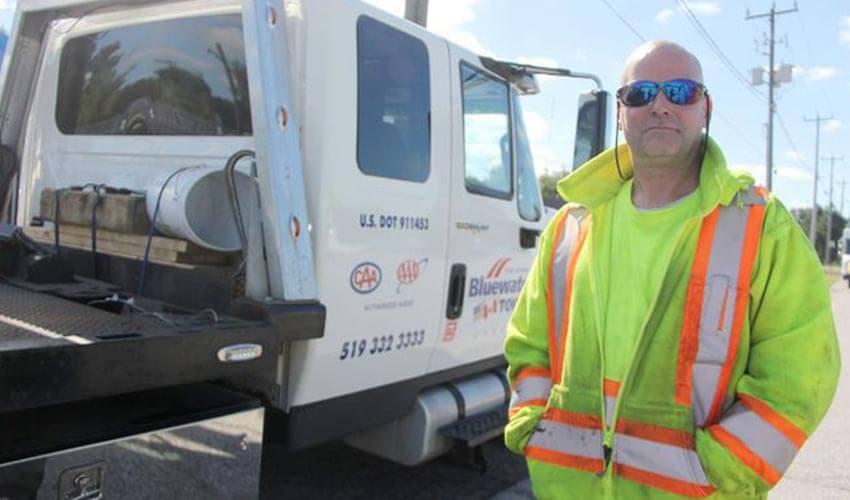 A man in a yellow vest standing in front of a white truck.