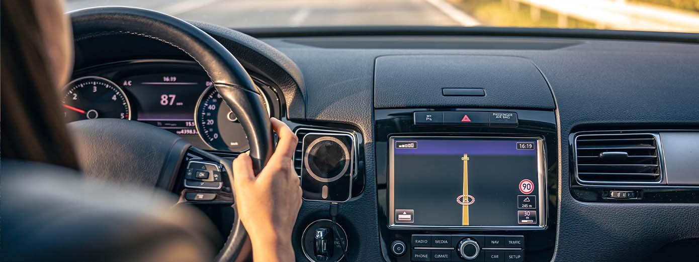 View from the driver’s seat of a moving car, showing a hand on the steering wheel, the dashboard reading 87 km/h, and a central GPS screen displaying a straight road with a 90 km/h speed limit and 245 meters to the next turn.