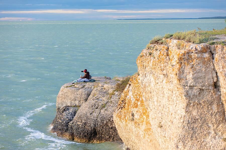 A man sitting on a cliff overlooking the ocean.
