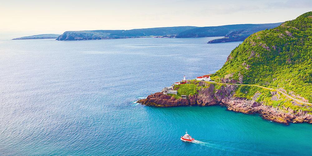 Aerial view of a lighthouse on a coastal headland with a boat passing by on a clear day.