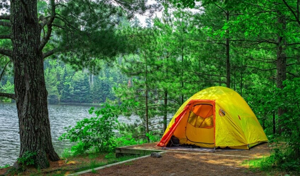 A yellow tent sits next to a lake in the woods.